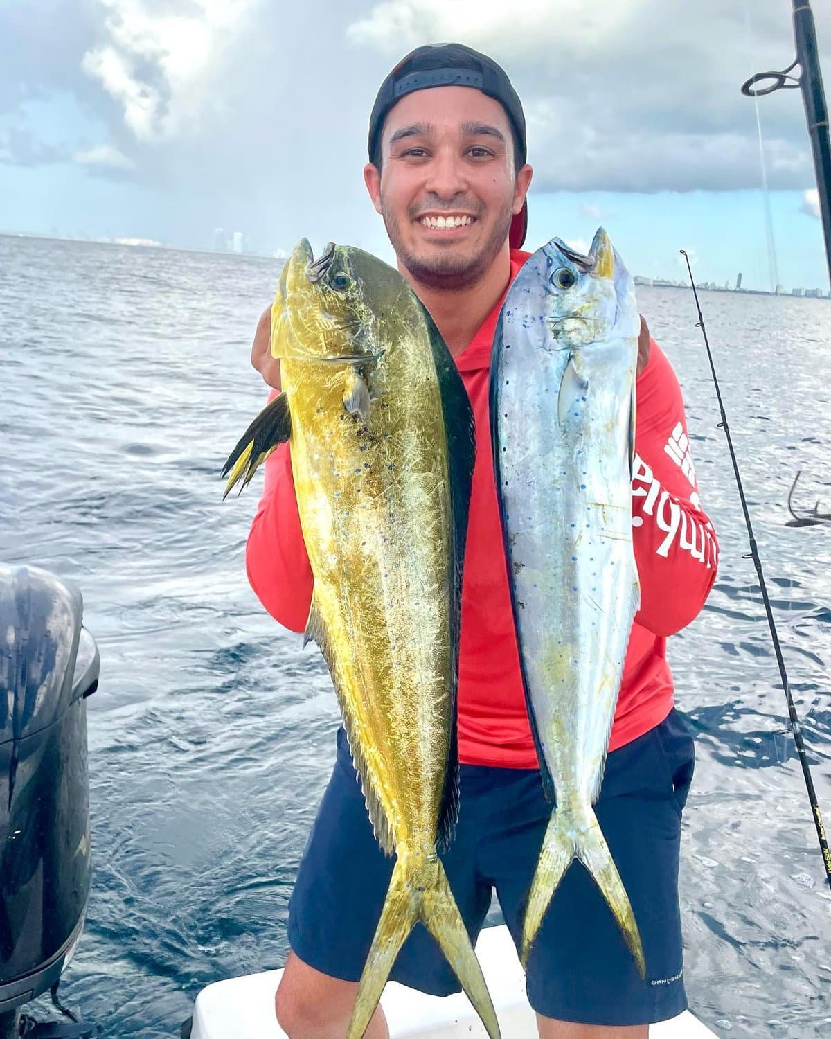 Smiling angler holding up two mahi mahi offshore