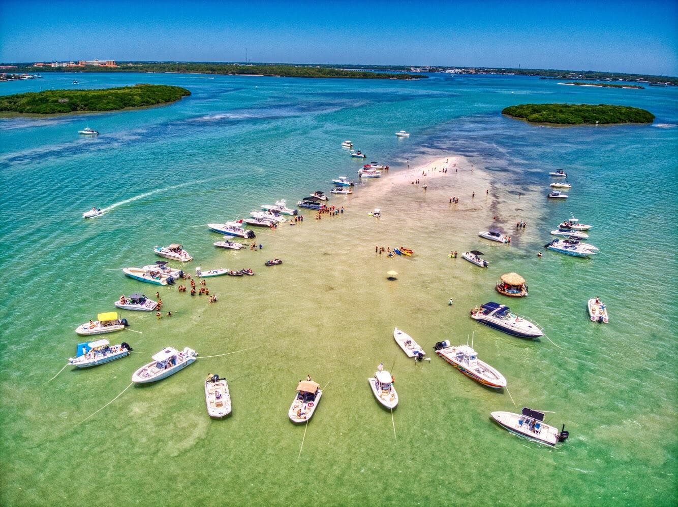 Boats anchored around a shallow sandbar in clear green water
